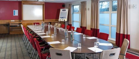 A conference room with a long table, red chairs, a whiteboard, and a projector.