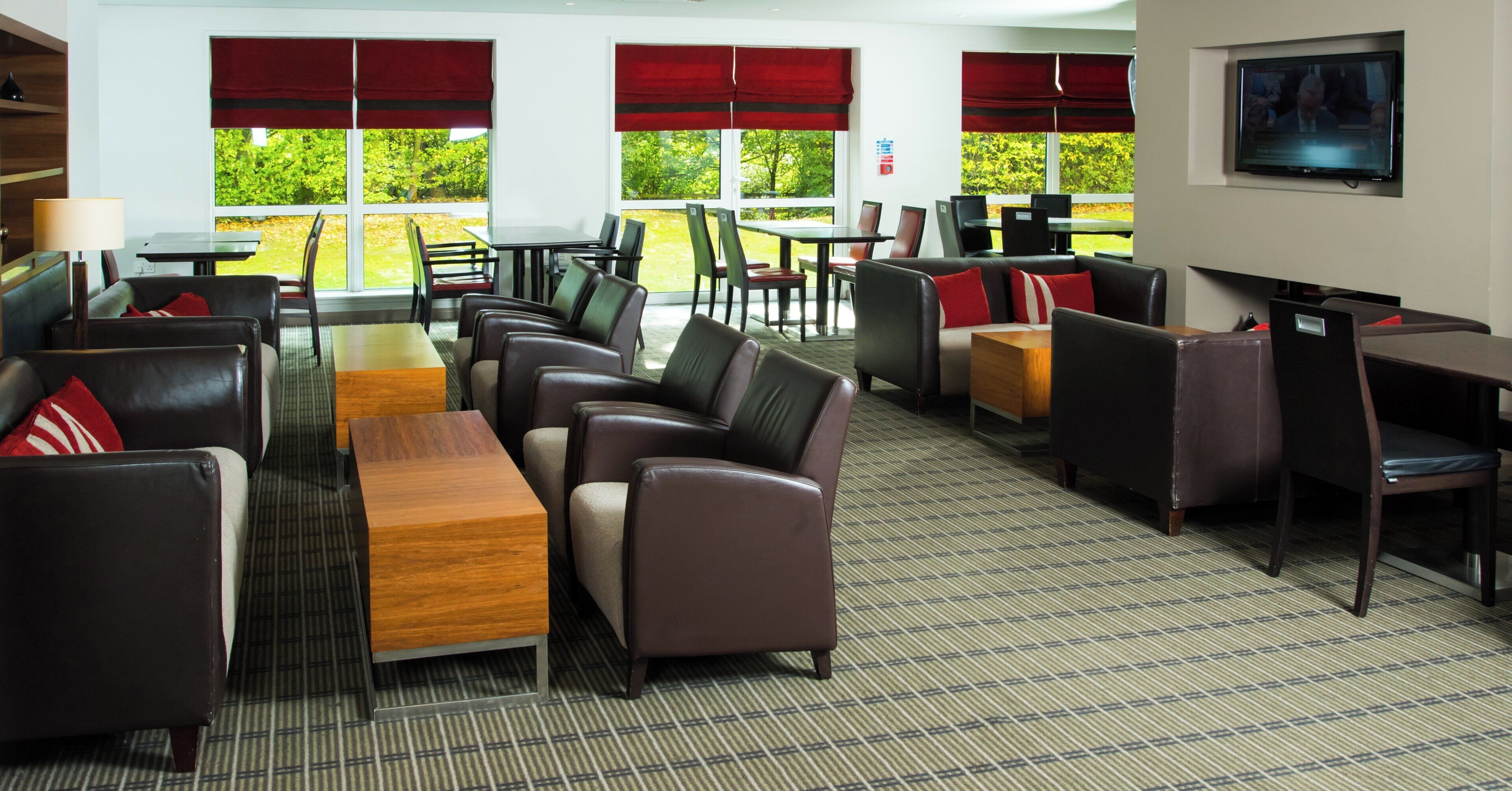 A hotel lobby with leather seating, a wooden table, and large windows with red curtains.