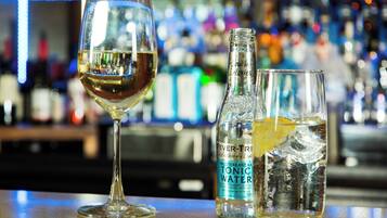 Un bar con una copa de vino blanco, una botella de agua tónica y un vaso con una rodaja de limón.