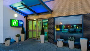 The exterior of a Holiday Inn Express hotel with a glass entrance, outdoor seating area, and a blue awning. - Holiday Inn Express Swindon - West by IHG (Swindon)