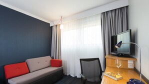 A hotel room with a sofa, a chair, a desk with a television, and a window with curtains. - Holiday Inn Express Swindon - West by IHG (Swindon)