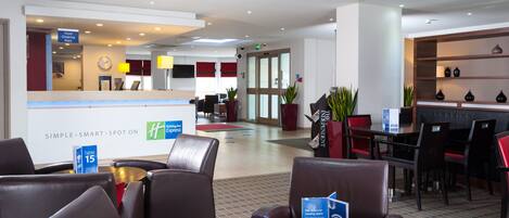 A hotel lobby with a reception desk, seating area, and a dining section.
