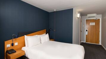 Ein Hotelzimmer mit einem großen Bett, einem Holznachttisch, einer Schreibtischlampe und einer Wand-Klimaanlage.