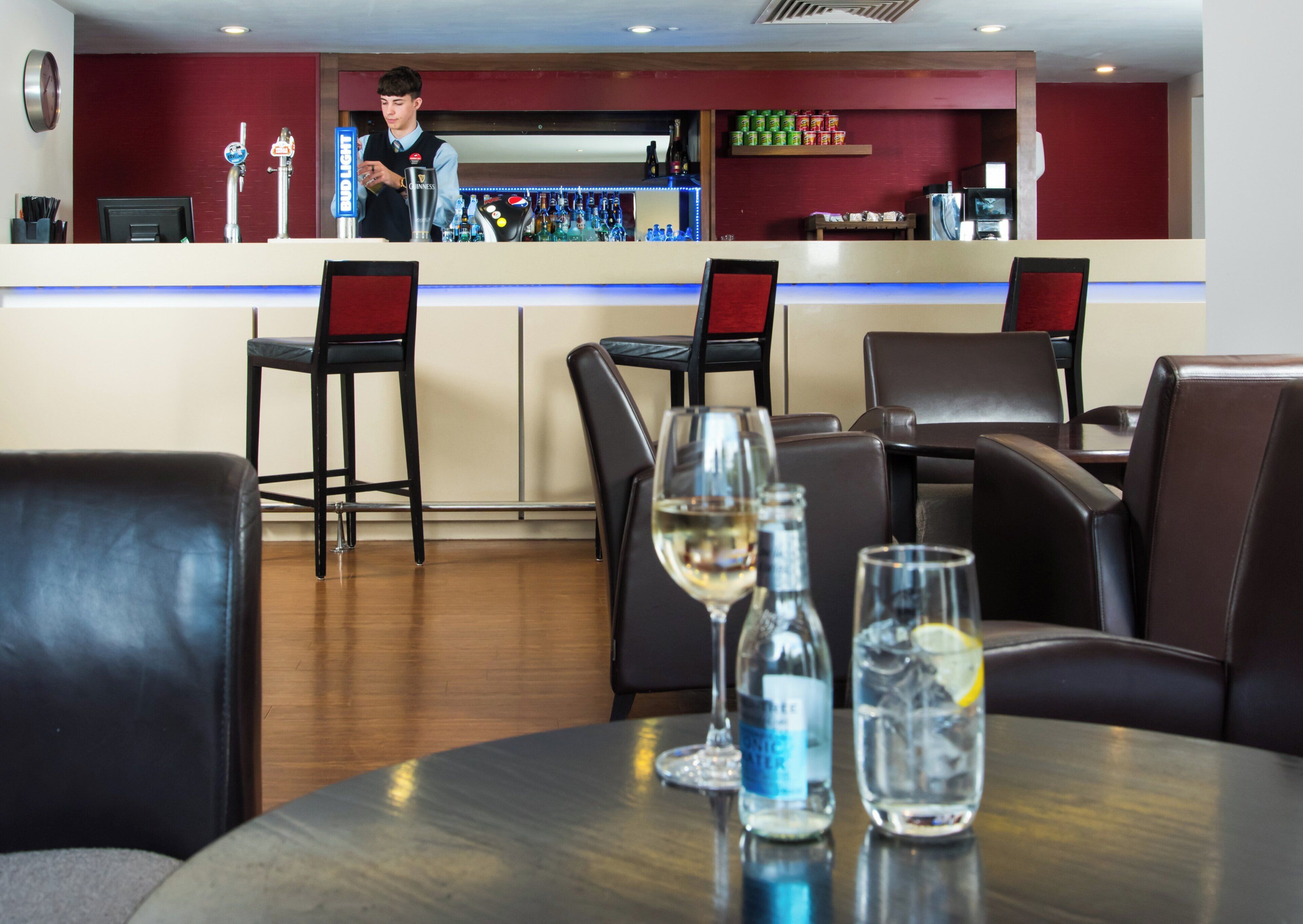 A bar area with a bartender, bar counter, seating with chairs, and a table with glasses and bottles.