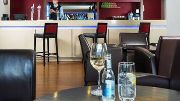 A bar area with a bartender, bar counter, seating with chairs, and a table with glasses and bottles.