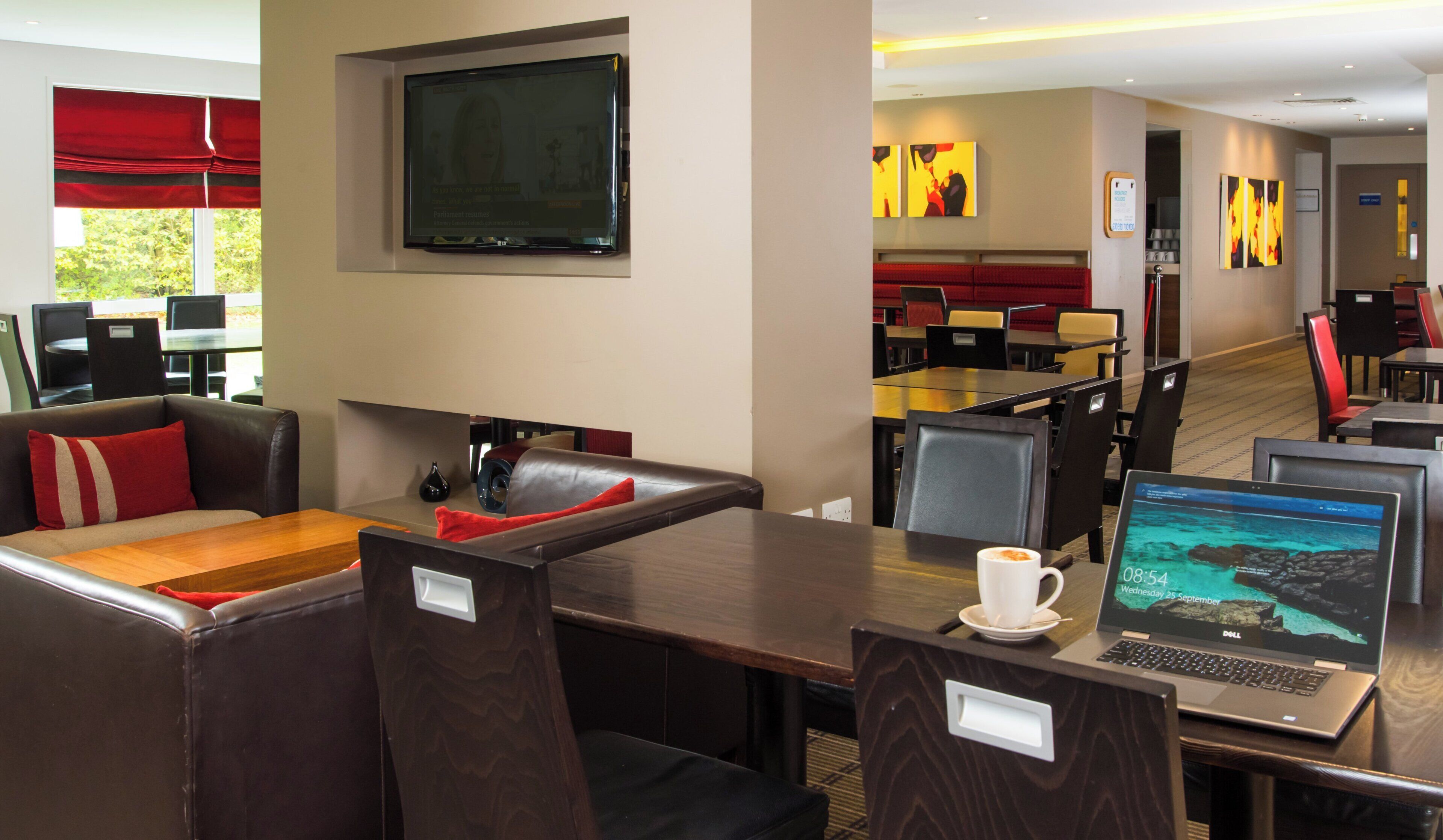 A hotel lobby with seating areas, a television, and a laptop on a table.