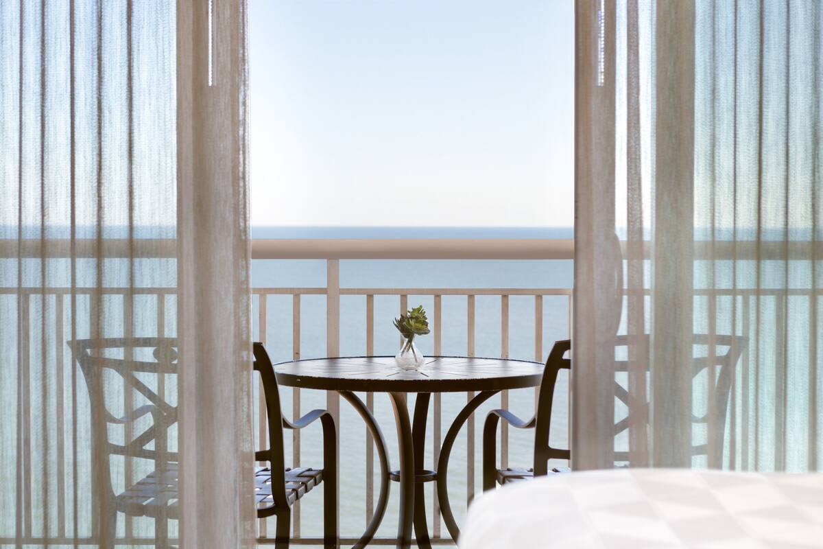 A balcony with a table and chairs, a small vase with a plant, and a view of the sea.
