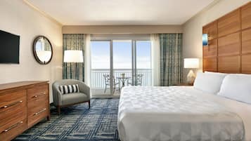 A hotel room with a large bed, a desk, a chair, a TV, and a balcony with a view.