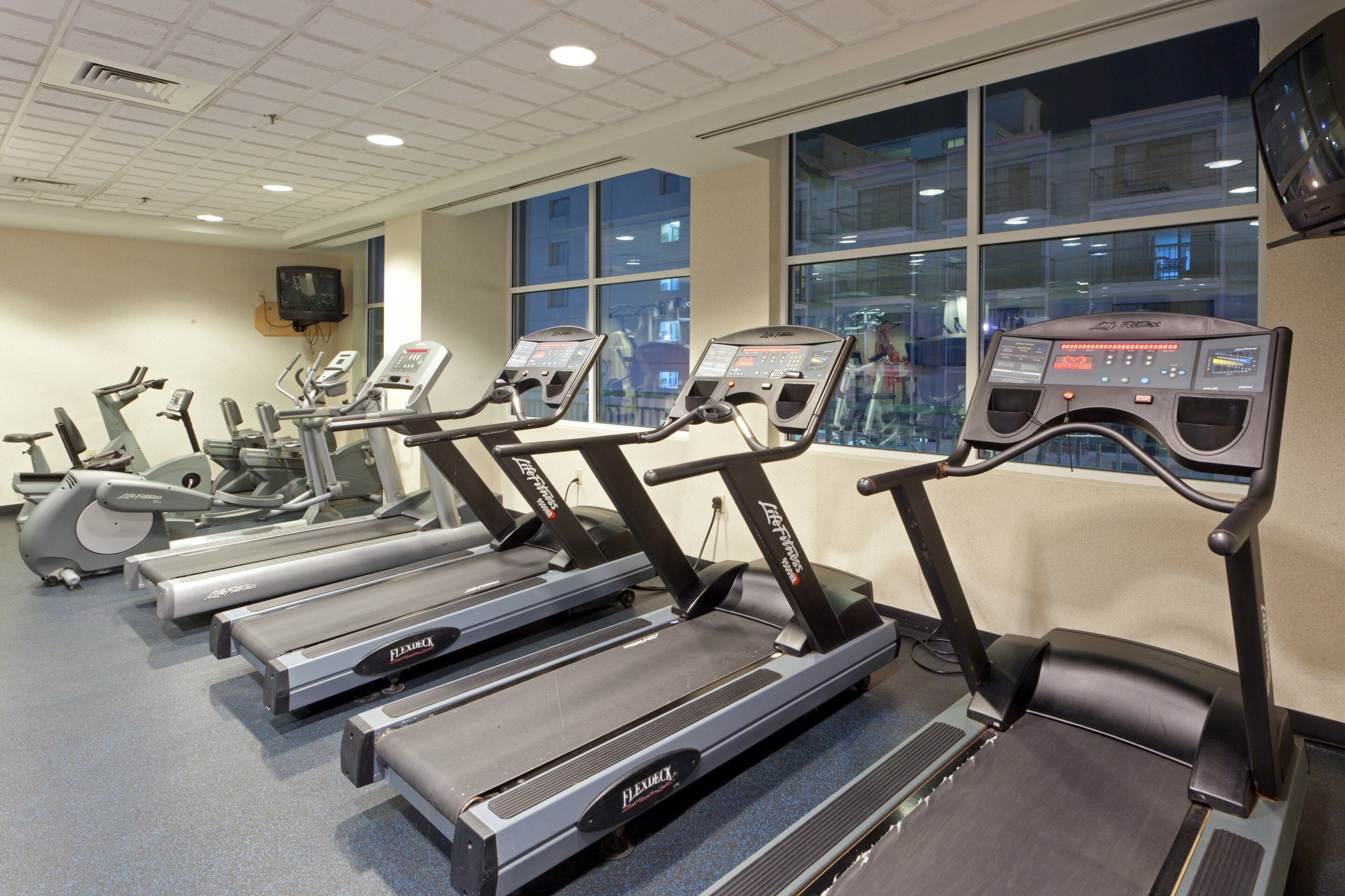 A gym with multiple treadmills, a television mounted on the wall, and large windows.