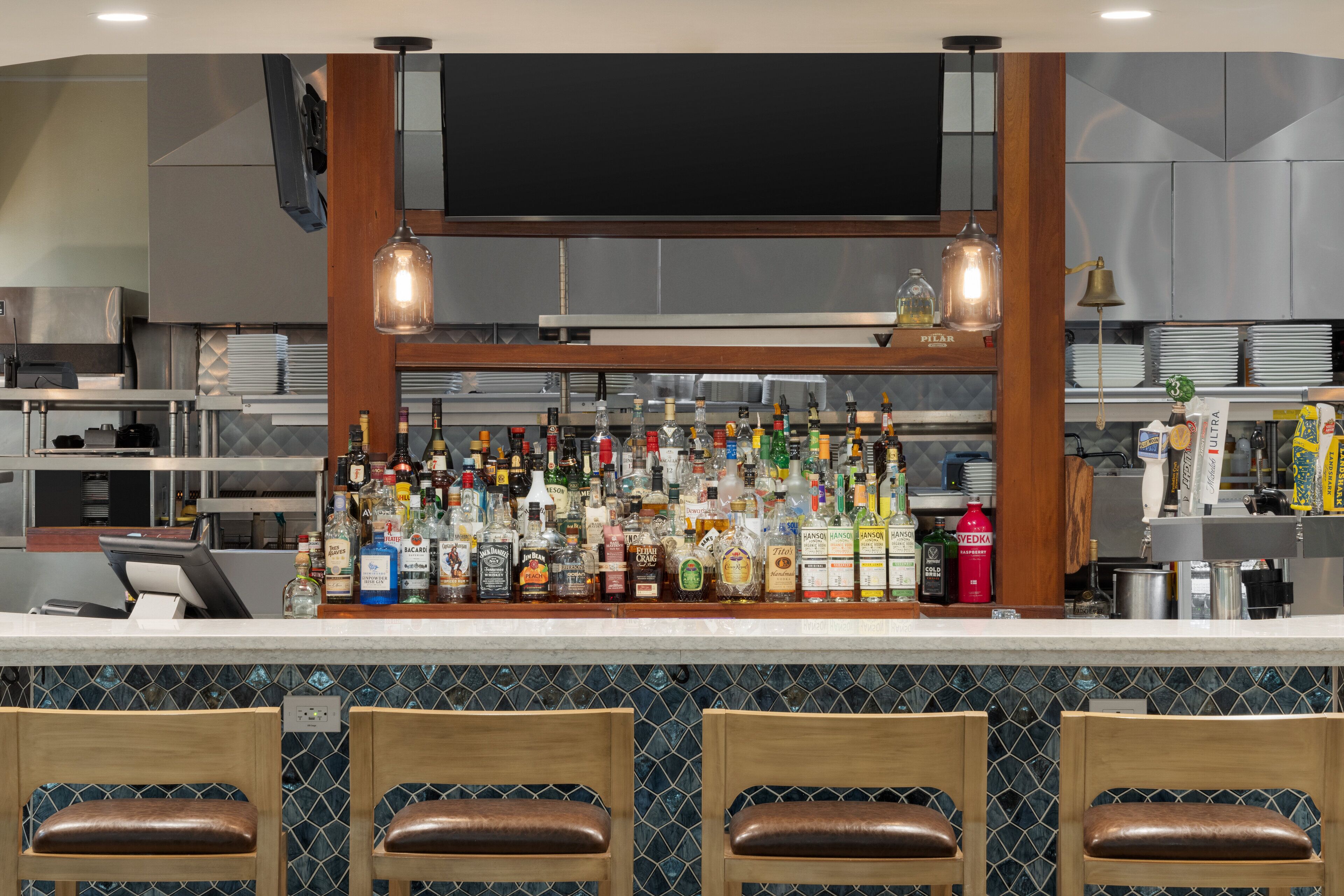 A bar area with a variety of liquor bottles, wooden chairs, and a television above the bar.