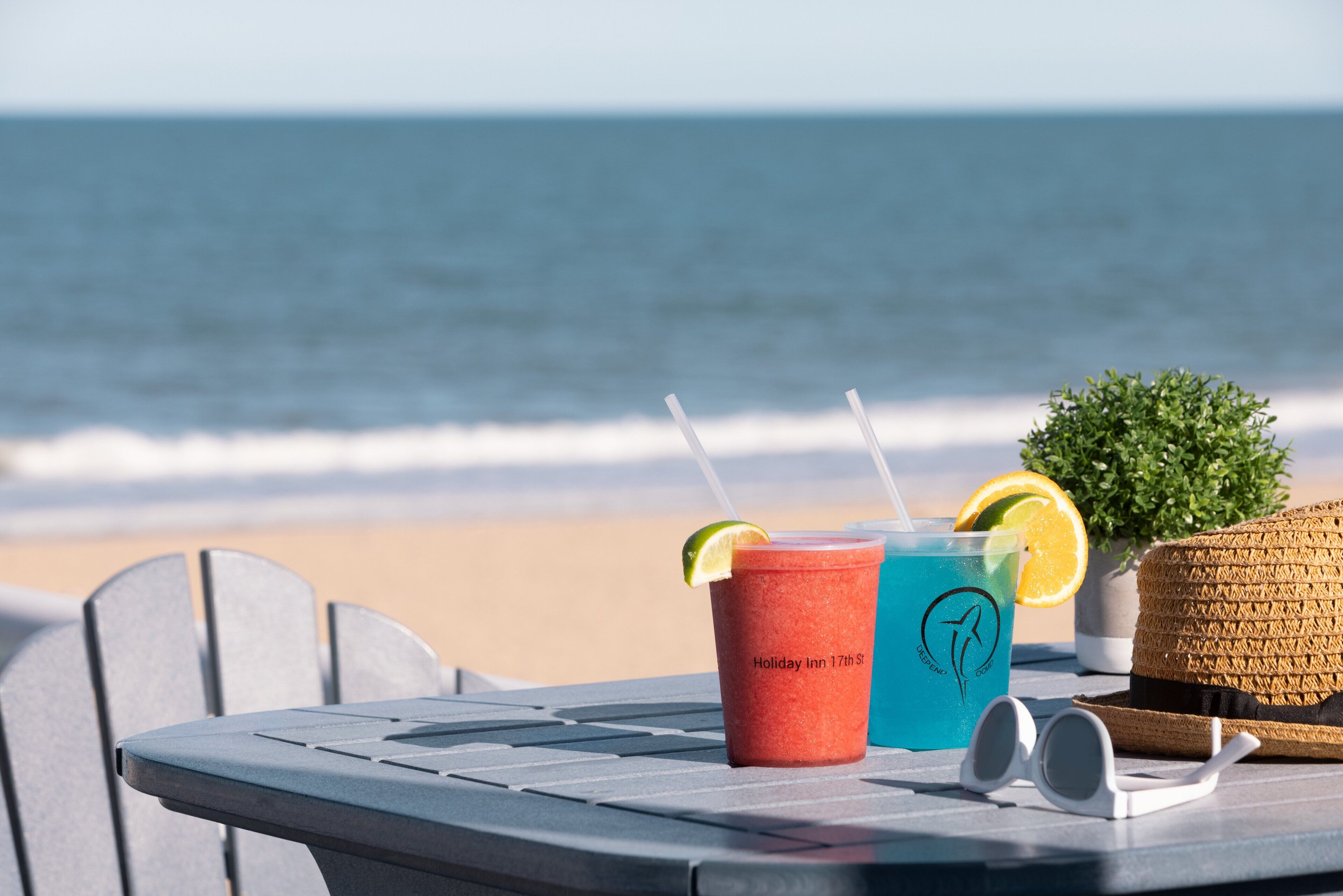 Ein Tisch mit Getränken, einem Hut und Sonnenbrille, mit dem Meer im Hintergrund.