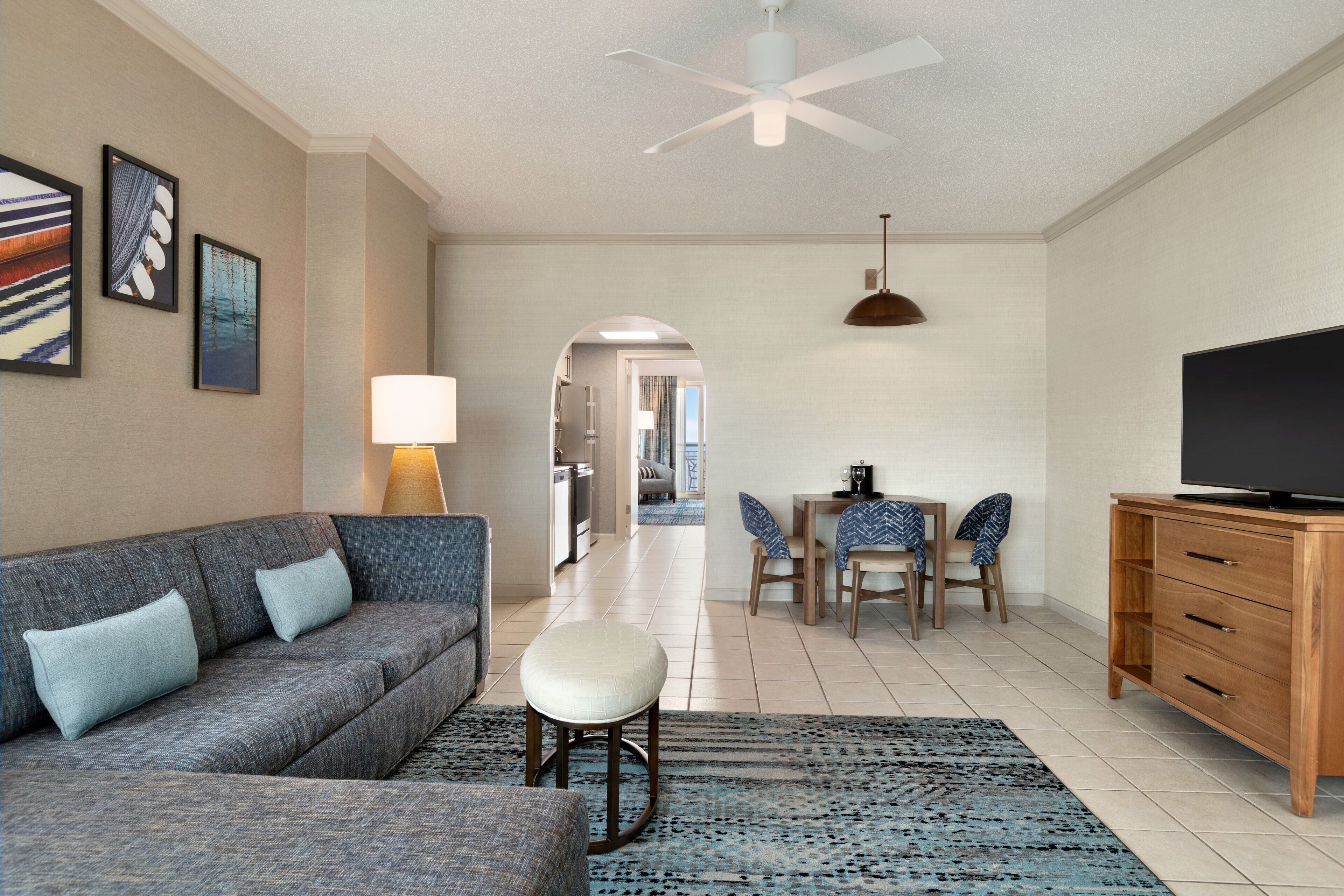 A modern living room with a sofa, ottoman, dining table, chairs, and a TV on a wooden cabinet.