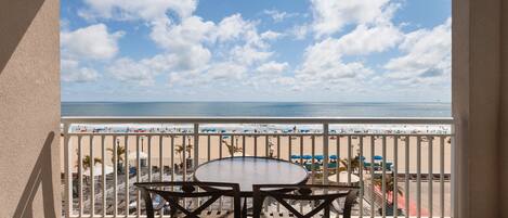 A balcony with a view of the beach, a round table, and chairs.