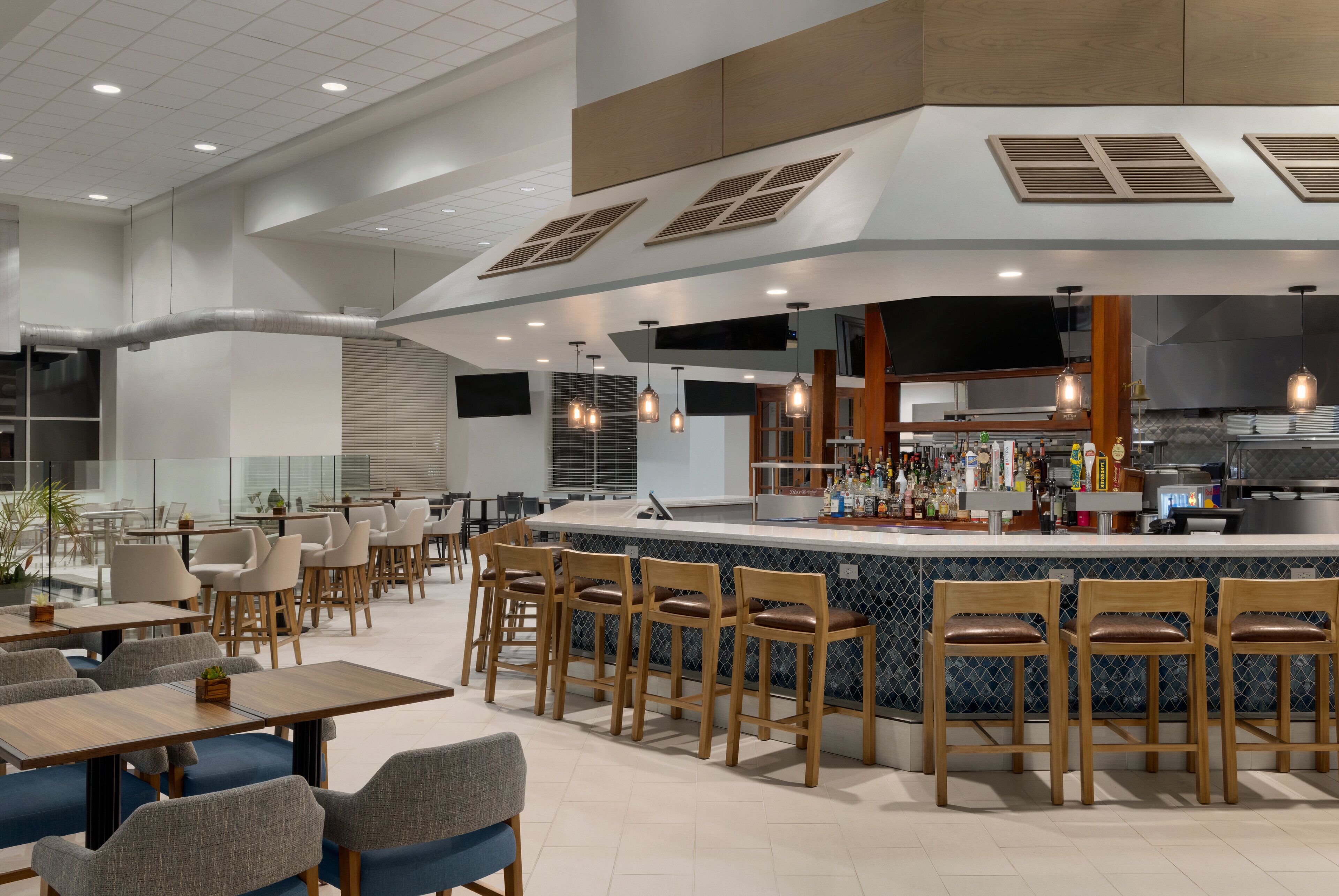 A modern restaurant with a bar area, multiple seating options, and a kitchen visible in the background.