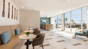 A modern lounge area with a sofa, round tables, and chairs, a bar area, and large windows with a view of palm trees and a beach. - Holiday Inn & Suites Ocean City by IHG (Ocean City)