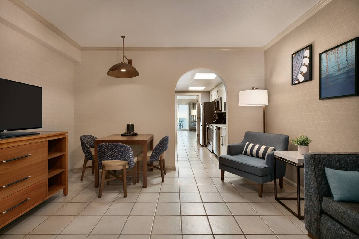 A modern living room with a TV, wooden furniture, a dining area, and a kitchen in the background.