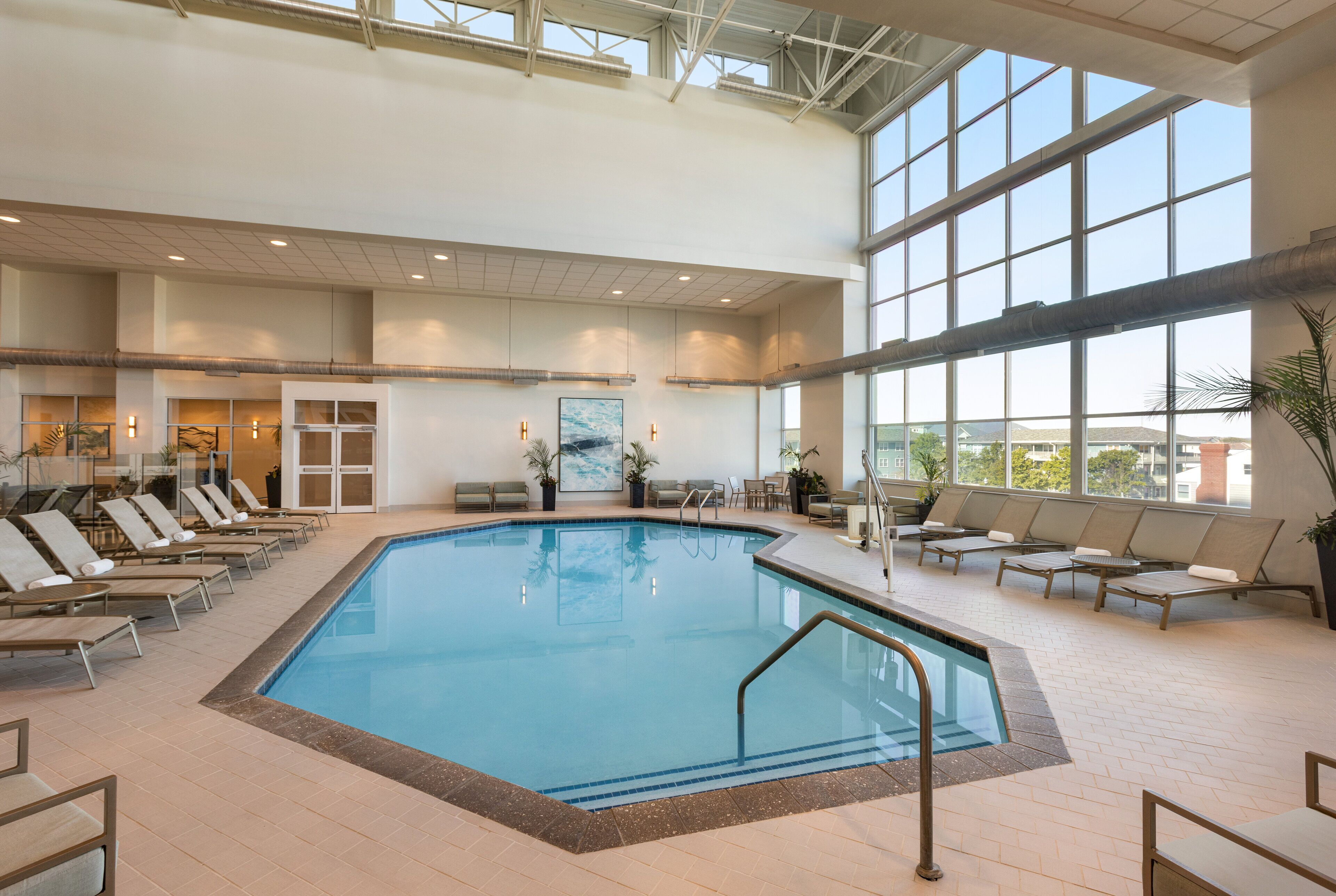 An indoor swimming pool with lounge chairs and a view of the city through large windows.