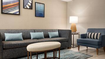 Un salon avec un canapé gris, un fauteuil bleu, une petite table ronde et une lampe.