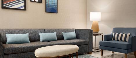 A living room with a grey sofa, a blue armchair, a small round table, and a lamp.