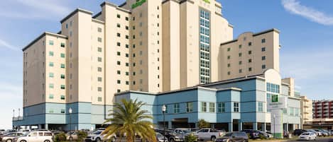 A multi-story Holiday Inn hotel with a modern design, featuring a prominent entrance and a parking lot with several cars.