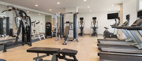 A gym with various exercise equipment, including treadmills, weight machines, and a bench.