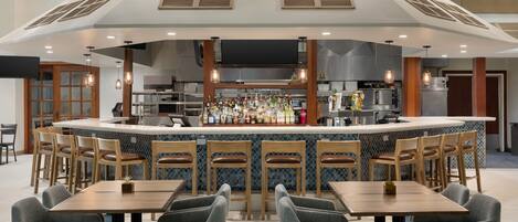 A modern bar area with a central island, bar stools, and a seating area with tables and chairs.