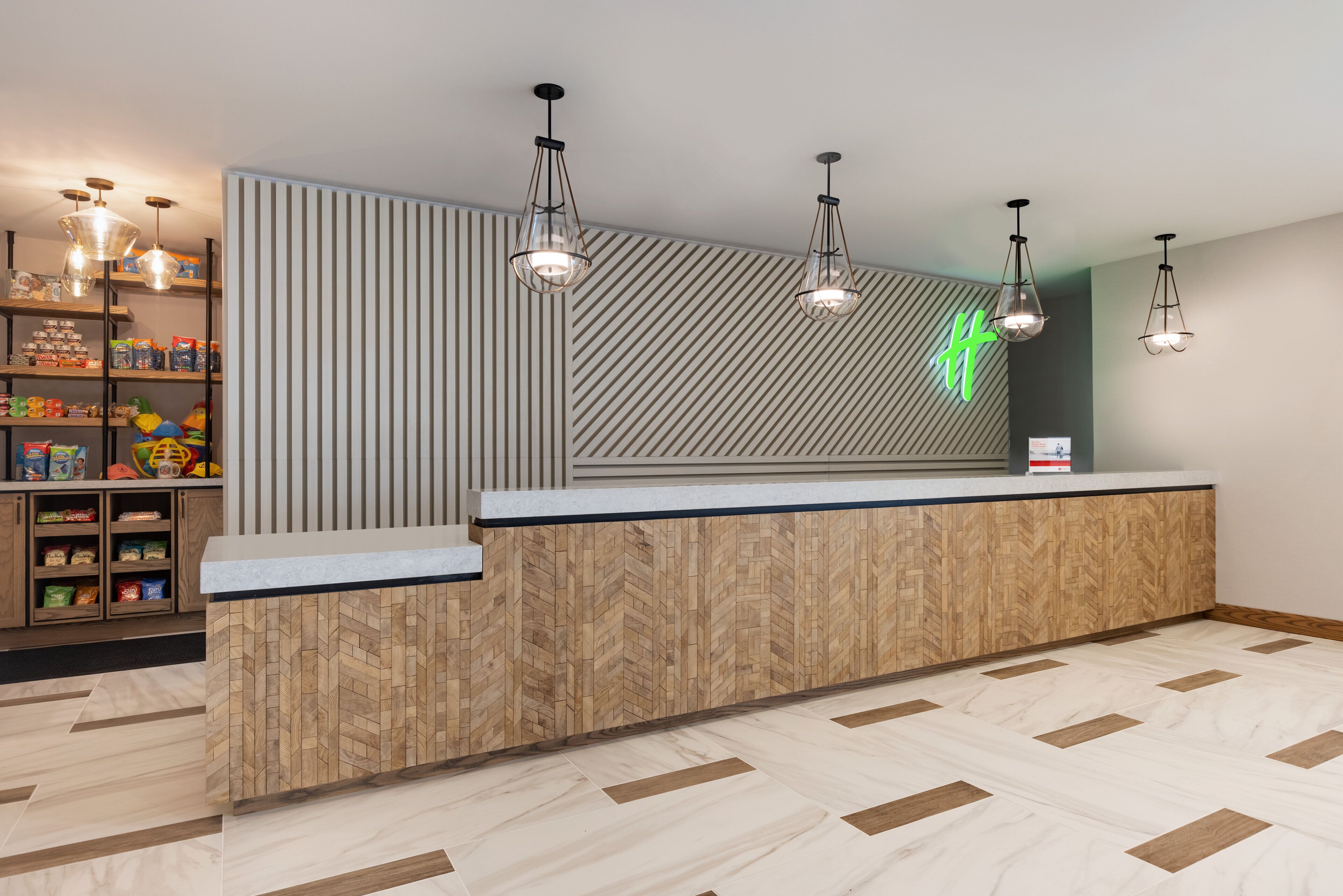 Zona de recepción con mostrador de diseño encalado, estanterías de madera con aperitivos e iluminación colgante.