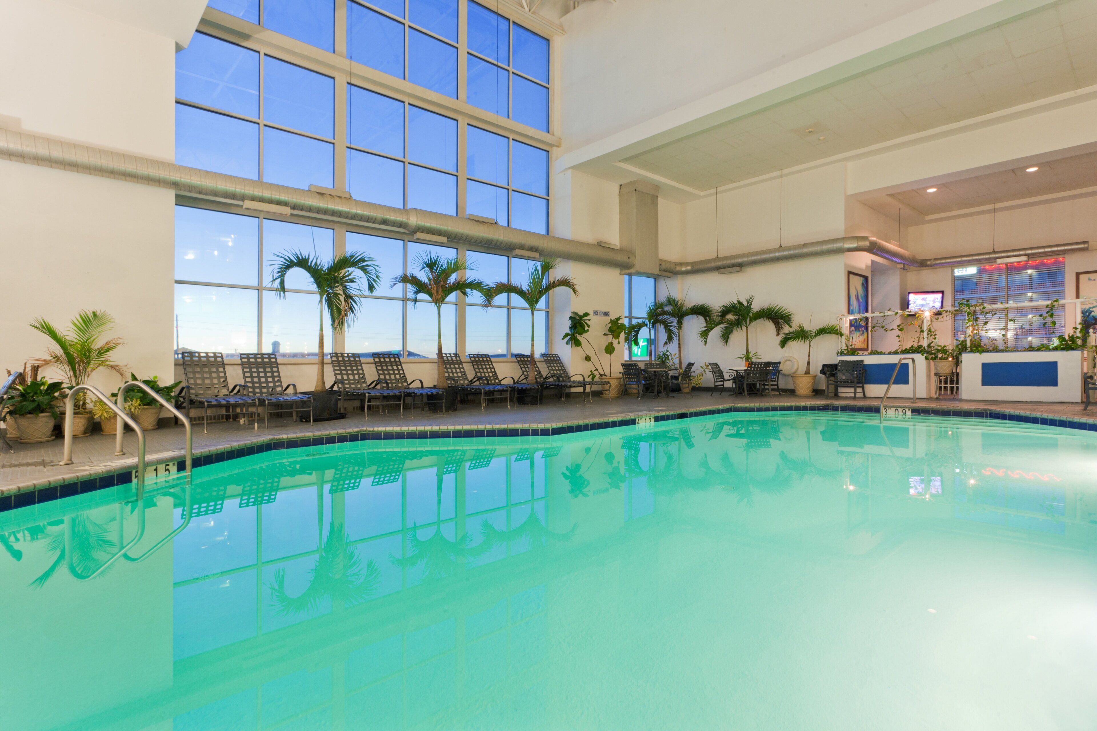 An indoor swimming pool with clear blue water, surrounded by lounge chairs and potted plants.