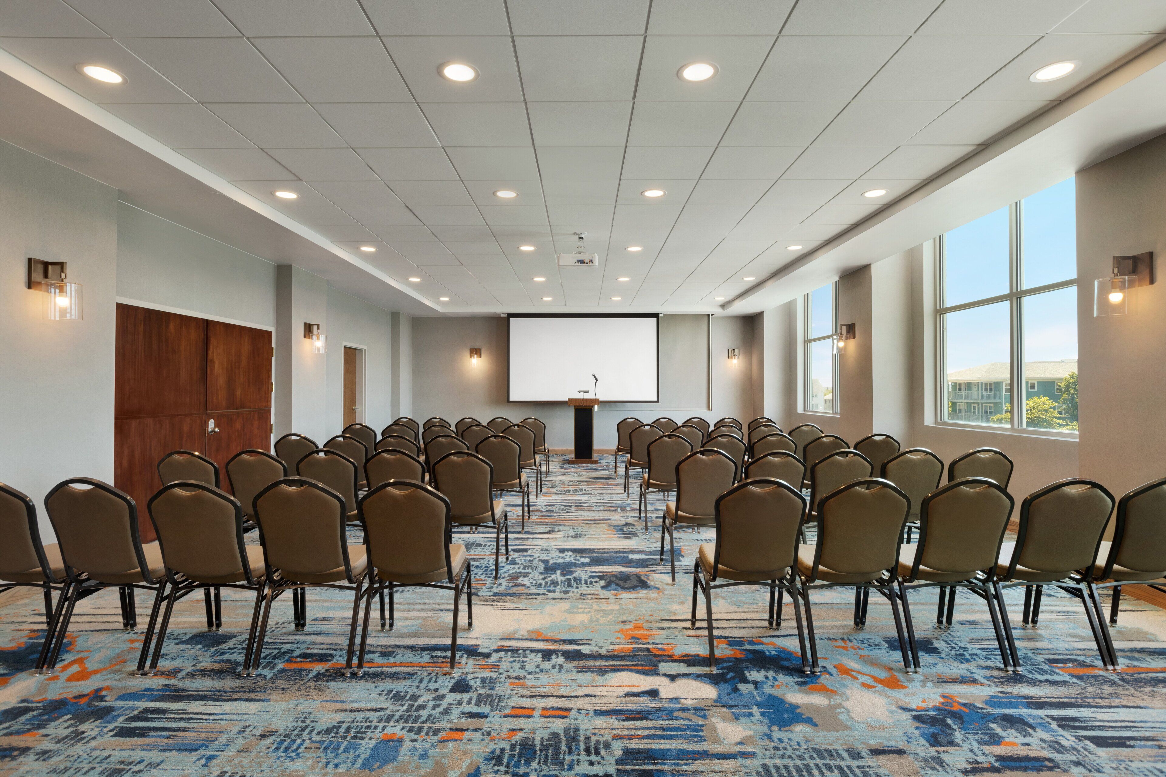 A conference room with rows of chairs facing a podium and a large screen.