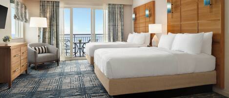 A hotel room with two beds, a desk, a chair, and a balcony with a view.