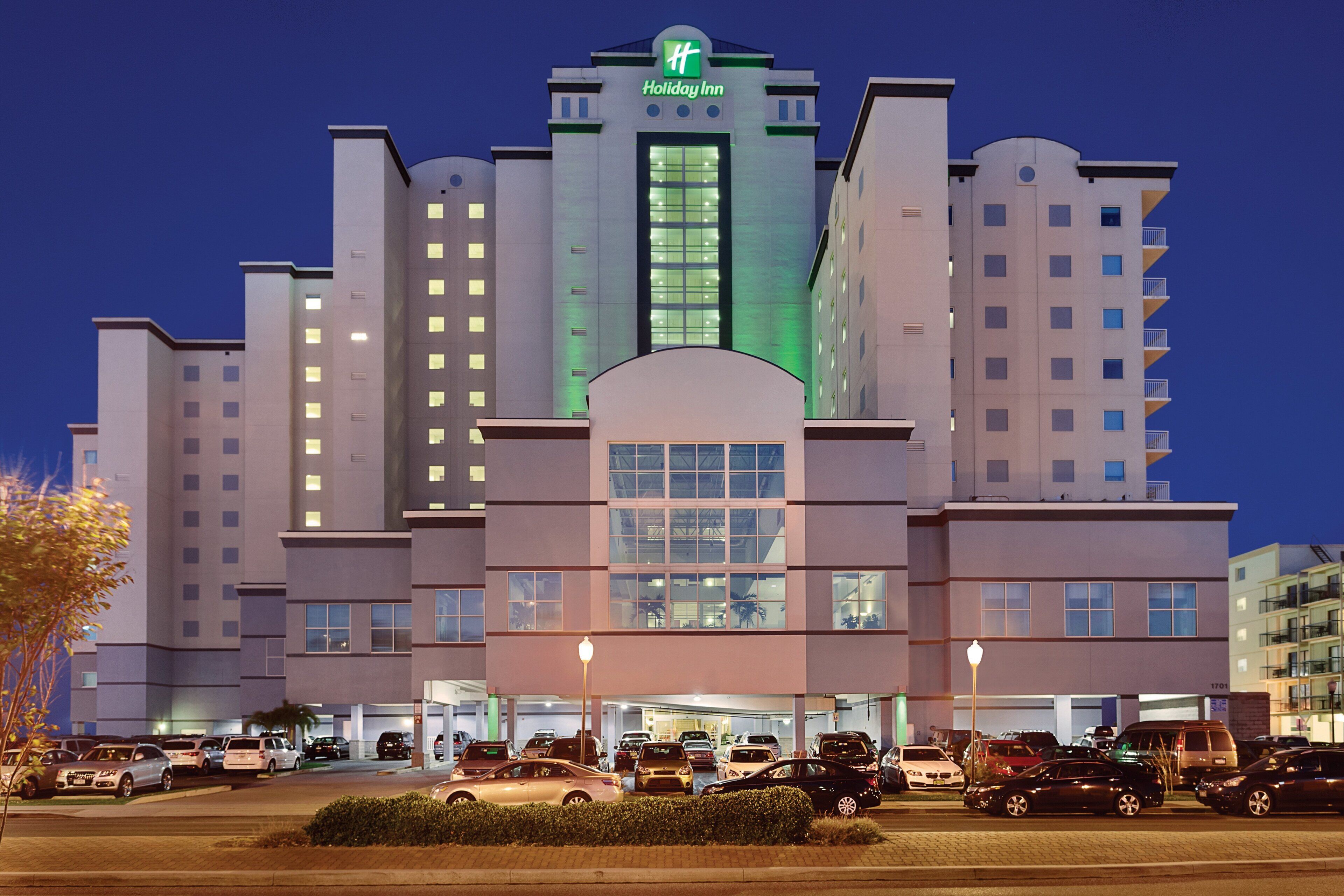 A Holiday Inn hotel with multiple floors, a central entrance, and a parking lot with various vehicles.