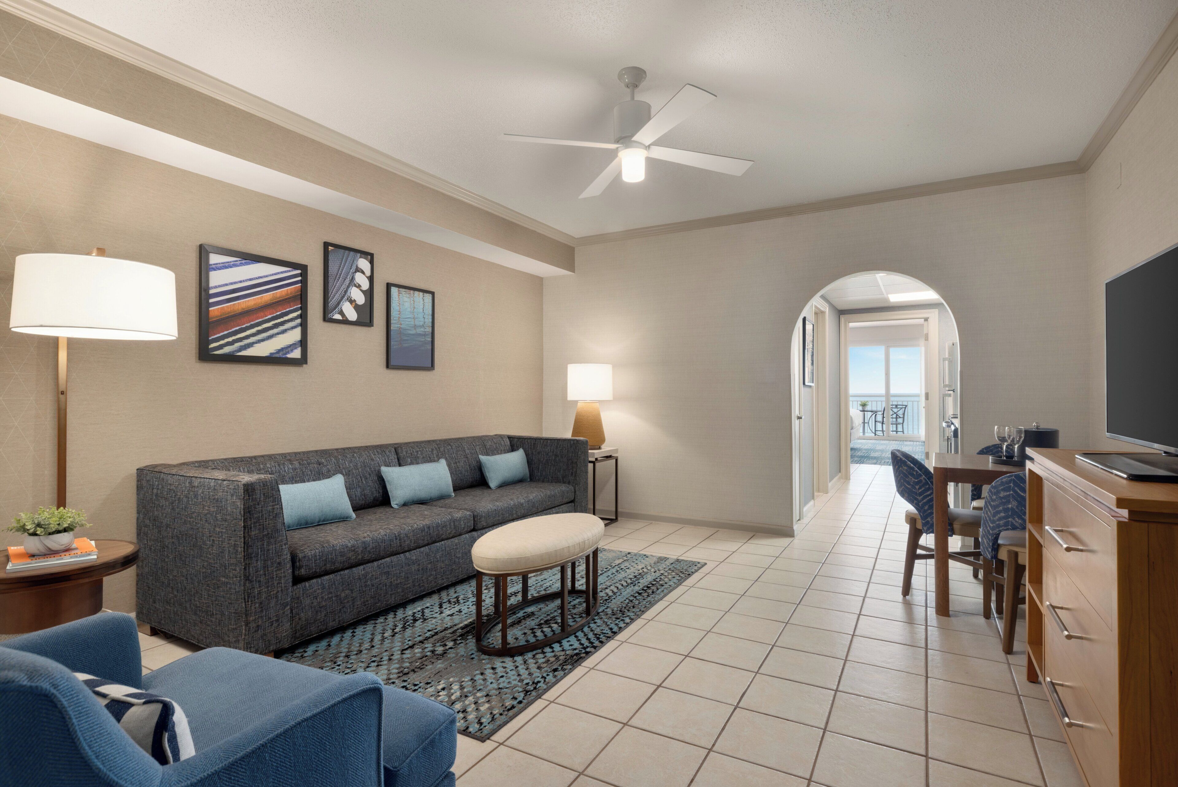 A modern living room with a sofa, armchairs, a coffee table, a TV, and a ceiling fan.