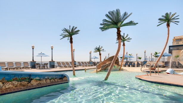 A clear pool with palm trees, lounge chairs, and umbrellas. - Holiday Inn & Suites Ocean City by IHG (Ocean City)