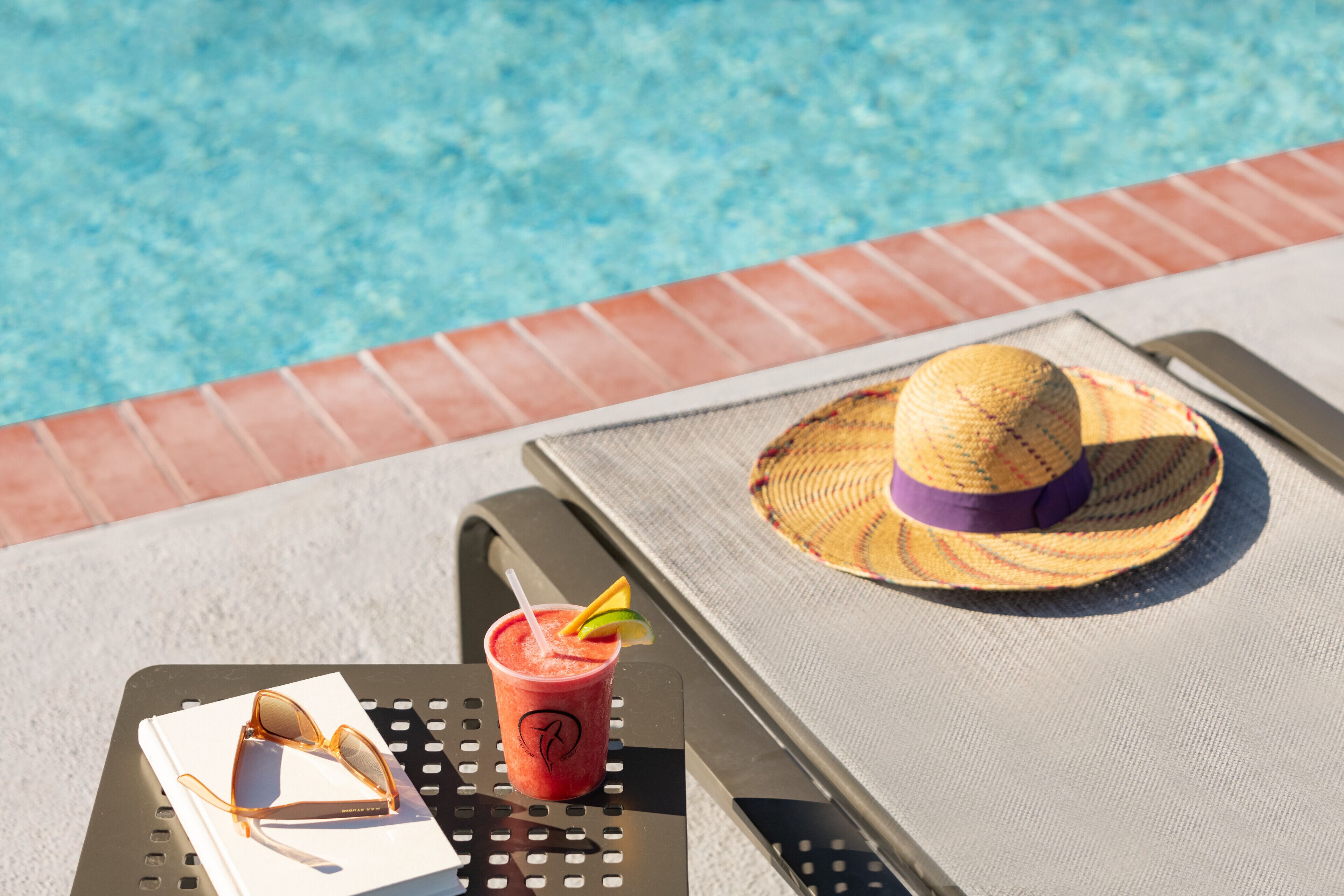 Un sillón junto a la piscina con una bebida, gafas de sol y un sombrero de paja.