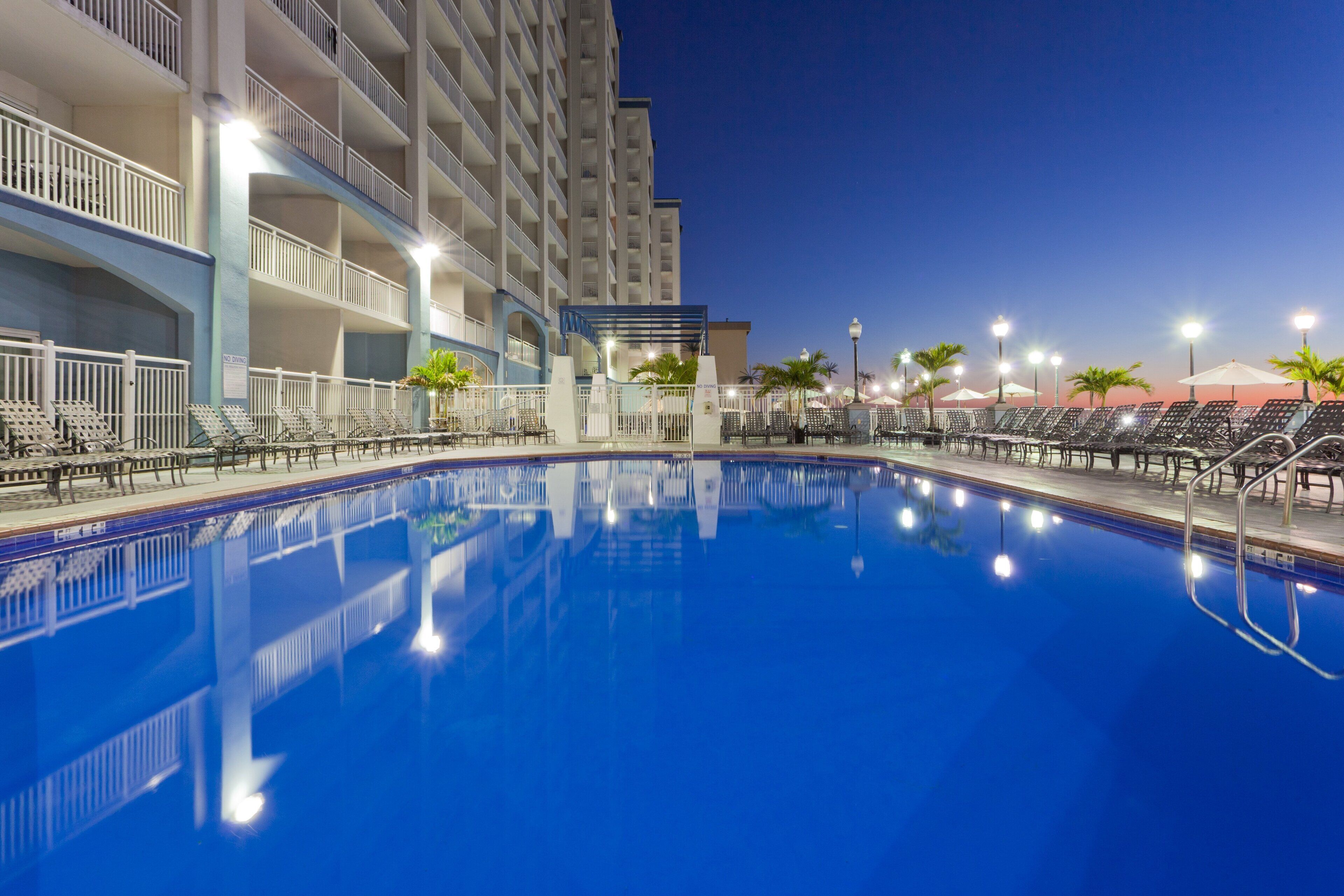 A swimming pool with lounge chairs and umbrellas, surrounded by a multi-story building with balconies.