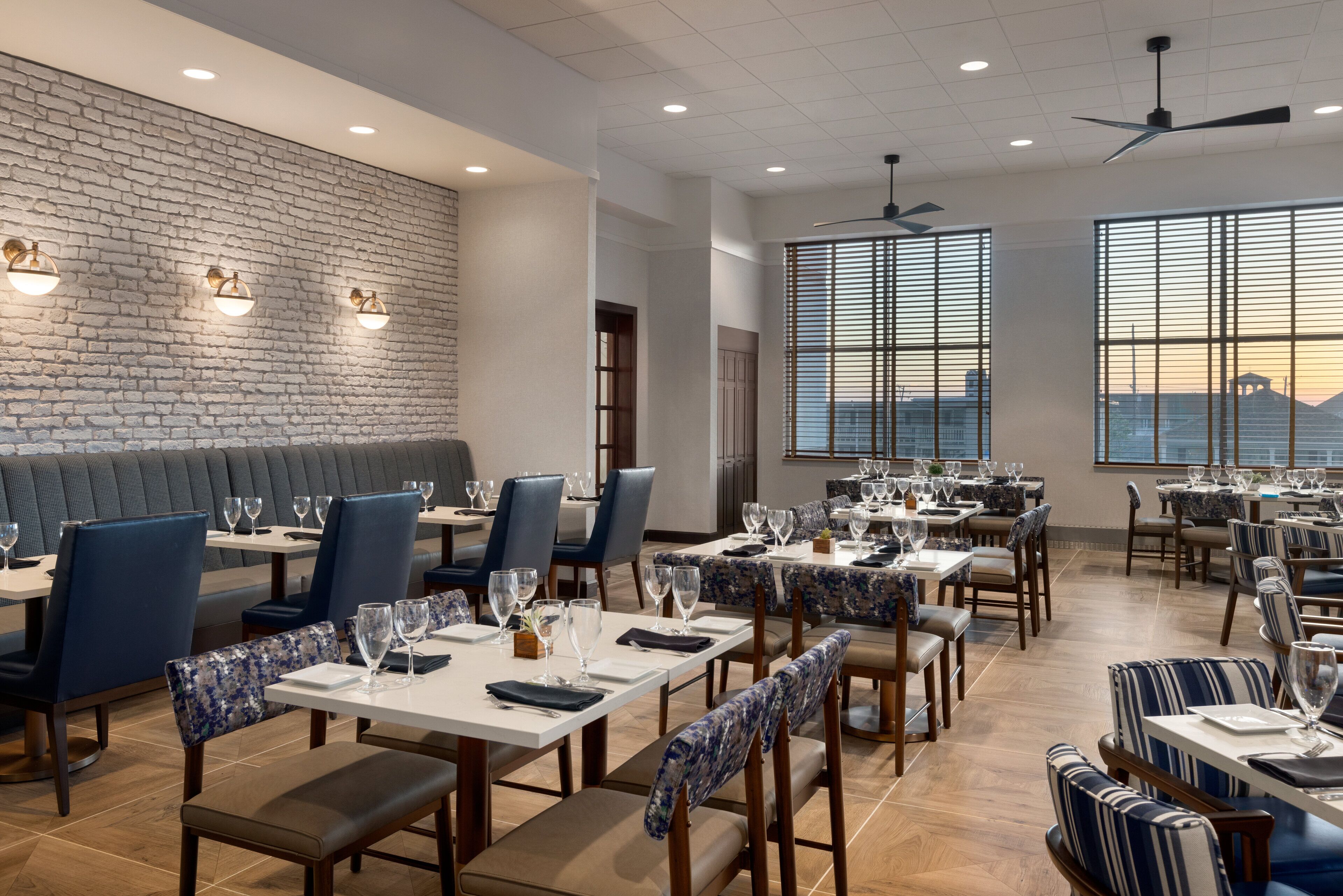 A restaurant with a brick wall, large windows, and a variety of seating arrangements including tables and booths.