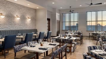 A restaurant with a brick wall, large windows, and a variety of seating arrangements including tables and booths.