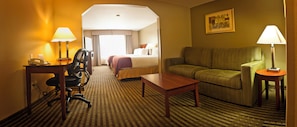 A hotel room with a bed, a sofa, a desk with a lamp, and a chair.
