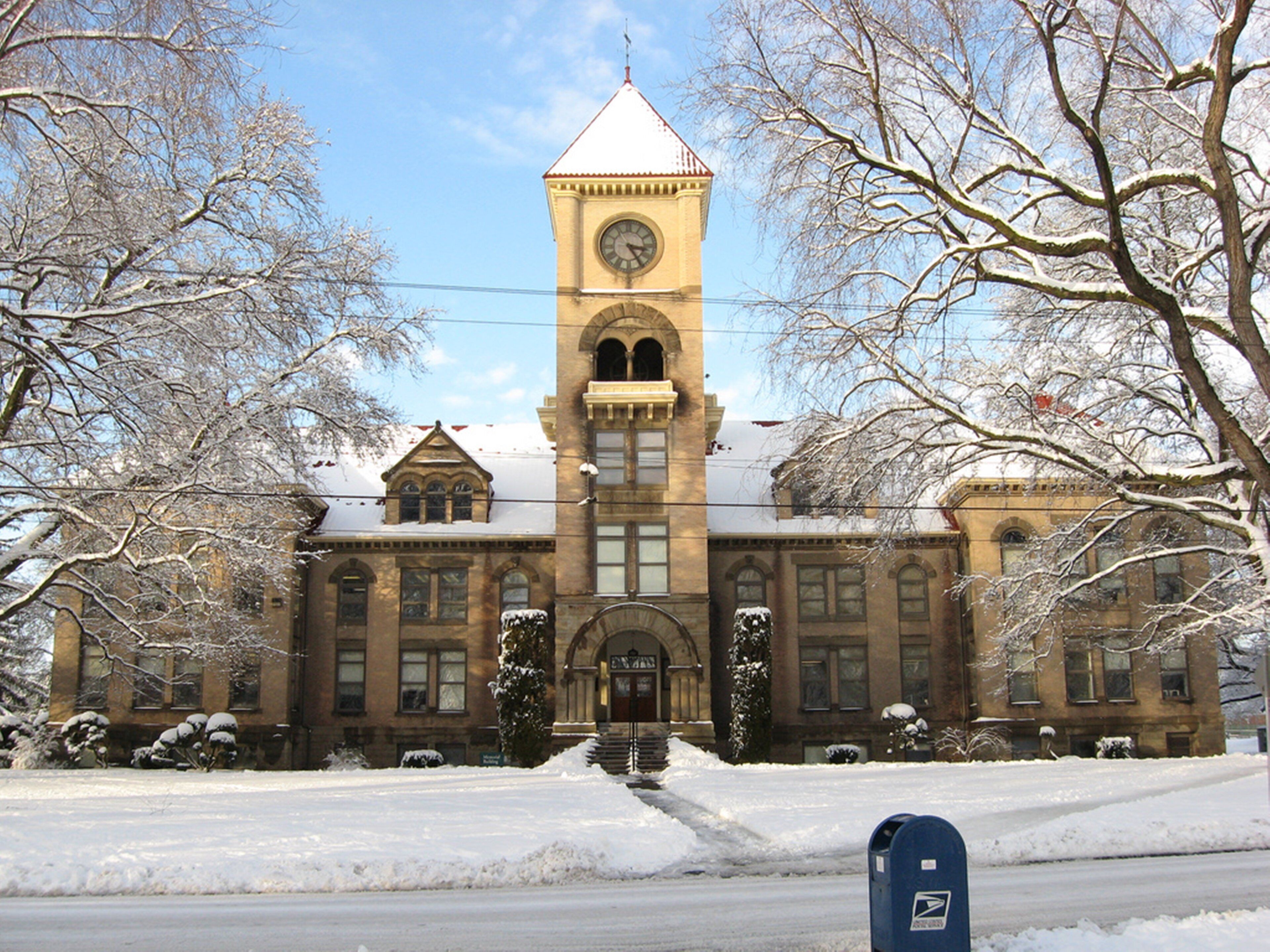 A historic building with a clock tower, arched windows, and snow-covered surroundings.