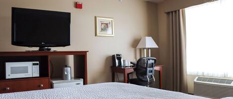 A hotel room with a bed, a television, a microwave, a coffee maker, and a desk with a chair.