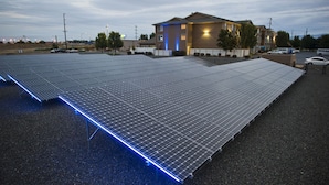 A large solar panel array installed on a flat surface, likely a parking lot, with a building in the background.