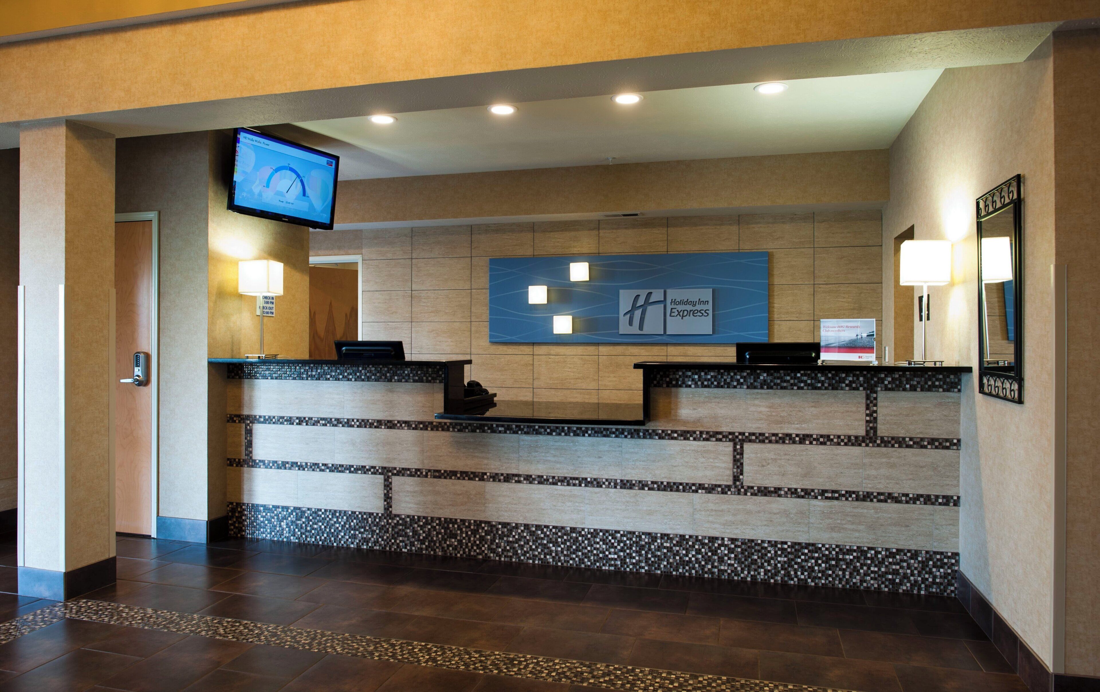 Un'area di ricevimento di un hotel con uno schermo digitale, una scrivania della reception e un cartello per Holiday Inn Express.