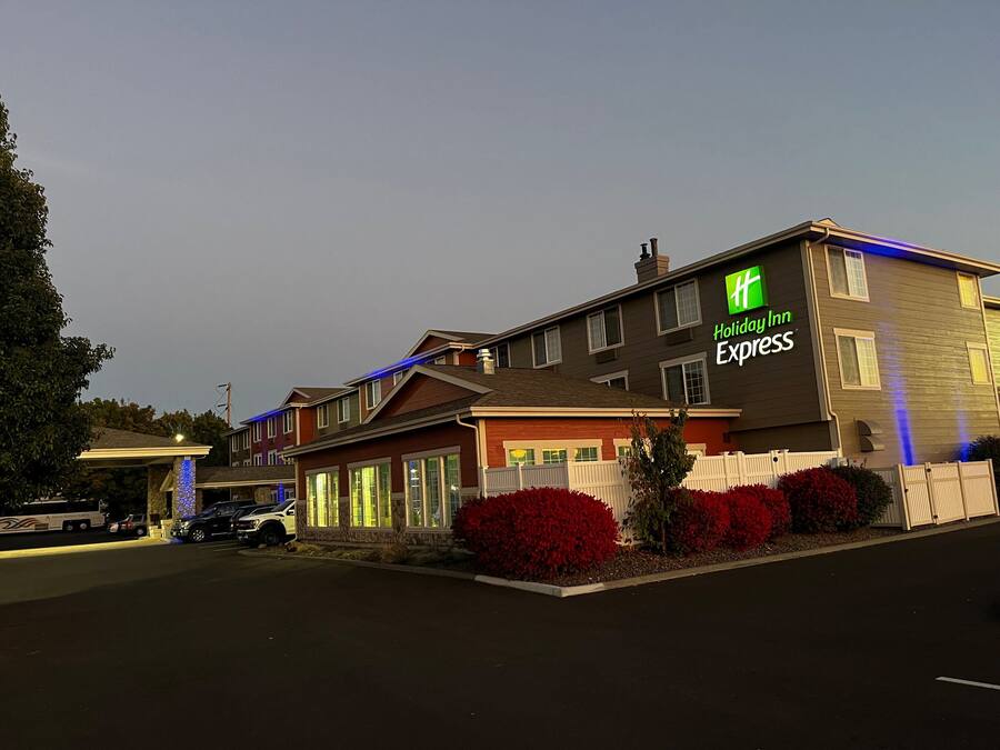 Un bâtiment de l’hôtel Holiday Inn Express avec une façade en pierre, de nombreuses fenêtres et un parking où sont stationnés des véhicules.