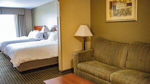 A hotel room with two beds, a sofa, a lamp, and a framed picture on the wall.