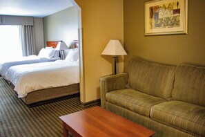A hotel room with two beds, a sofa, a lamp, and a framed picture on the wall.