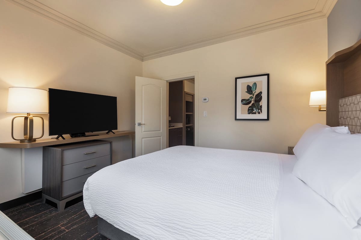 A hotel room with a bed, a television on a stand, a desk with drawers, a door to a closet, and a framed picture on the wall.