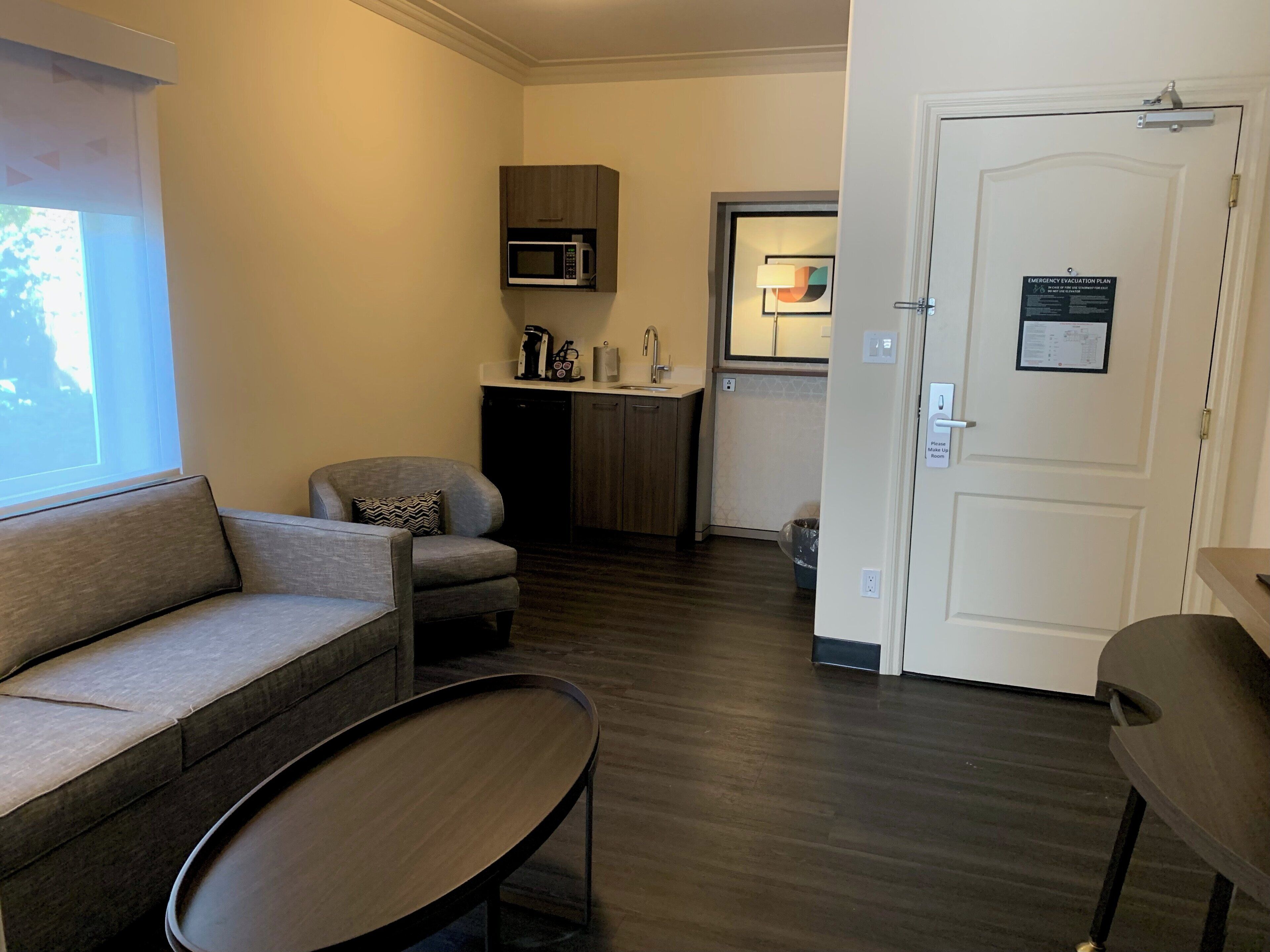 A compact living space with a sofa, a small table, a microwave, and a door with an emergency evacuation plan.