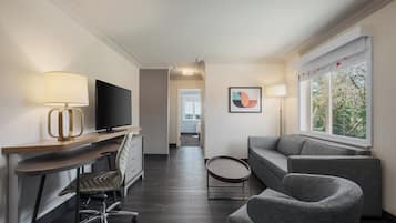 Ein modernes Hotelzimmer mit Schreibtisch, Stuhl, Fernseher, Sofa und einem Fenster mit Blick.