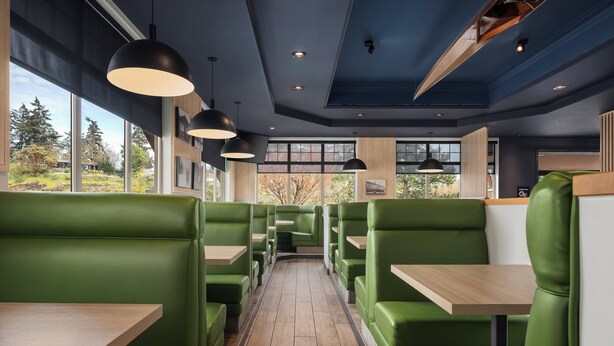 A restaurant with green booths, wooden tables, and pendant lighting.