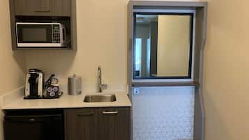 Cocina compacta con microondas, cafetera, lavamanos y un ventanal pequeño.